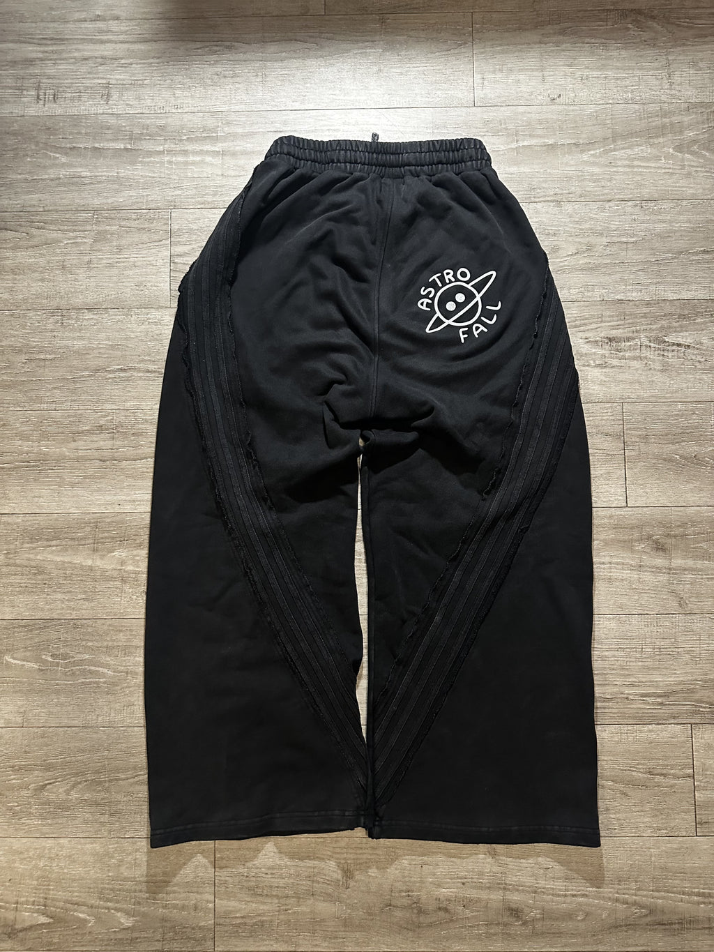 Black pants with a logo on the back, laid flat on a wooden floor.